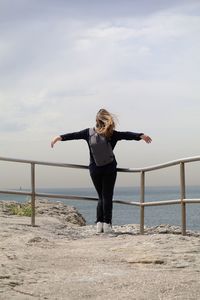 Full length of woman with arms outstretched standing at observation point against sky