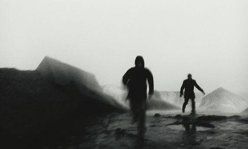 Rear view of silhouette people walking on sand against sky