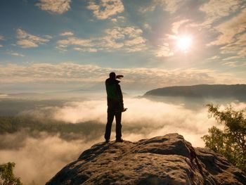 Professional photographer with tripod in hands on cliff and thinking. misty sunrise in valley below