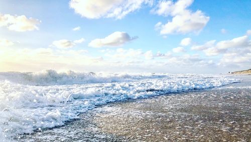 Waves rushing towards shore against sky