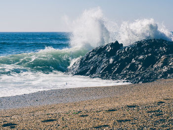 Waves splashing on rocks at shore against clear sky