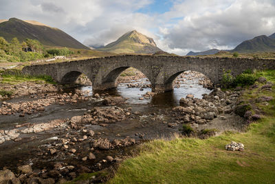 Old stone arch bridge over a river at sligachan on the isle of skye, cuillin mountains rising behind