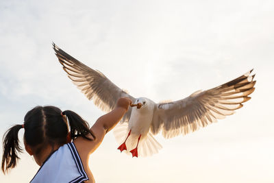 Low angle view of bird flying over girl against sky