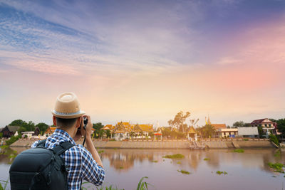 Rear view of woman photographing against sky during sunset