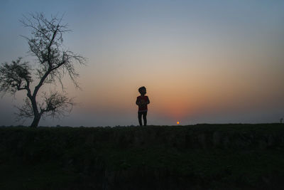 Silhouette man standing on field against sky during sunset