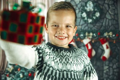 Portrait of smiling boy holding gift against christmas tree