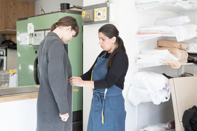 Mature female entrepreneur assisting young customer in overcoat at laundromat