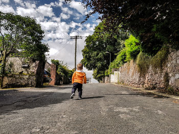 Man walking on road amidst trees against sky