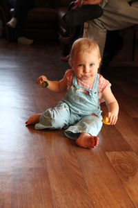 High angle portrait of cute baby sitting on hardwood floor at home