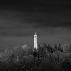 Low angle view of tower amidst trees against cloudy sky