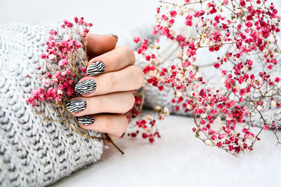 Hand in sweater and pink flowers with zebra animal printed nails. female manicure. glamorous 