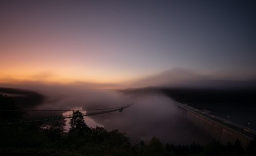 Bridge over silhouette trees against sky during sunset