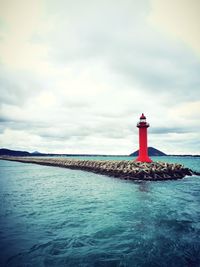 Lighthouse by calm sea against cloudy sky