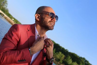 Thoughtful mid adult man wearing red suit and sunglasses against clear blue sky