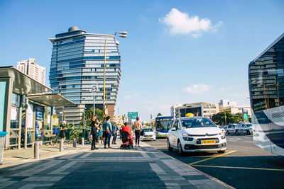 People walking on road by buildings in city against sky