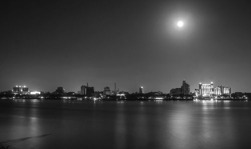 Illuminated city by river against sky at night