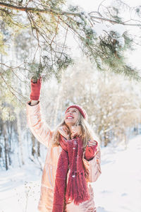 Happy young woman enjoying by trees on snowy field in winter