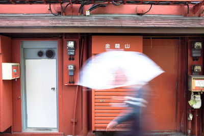 Blurred motion of man holding umbrella while walking against building