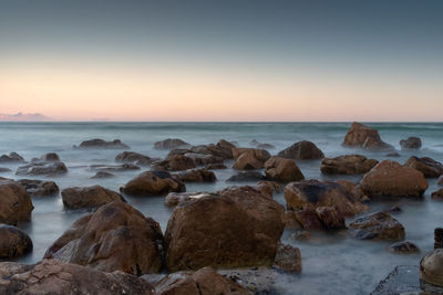 Rocks on beach against sky during sunset