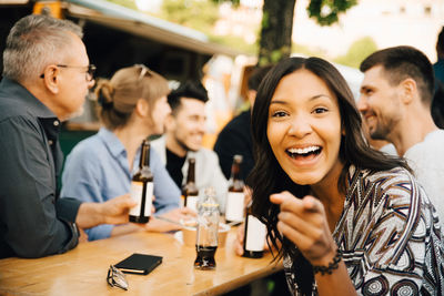 Portrait of smiling young woman pointing while sitting friends and enjoying at social gathering