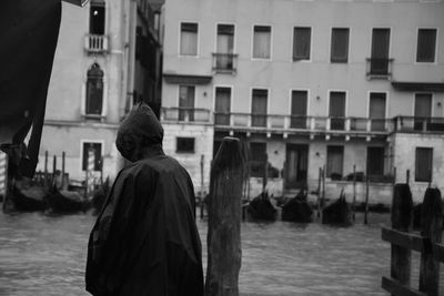 Man in hooded jacket standing by river in city