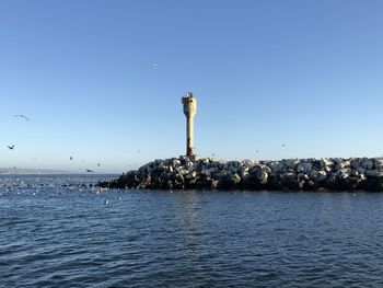 Lighthouse by sea against clear sky
