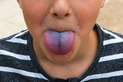 Midsection of boy sticking out tongue outdoors