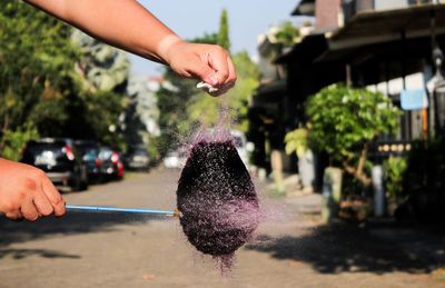 Cropped hands bursting water bomb over road