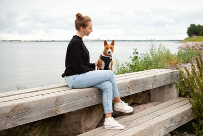 Full length of young woman sitting on pier against lake
