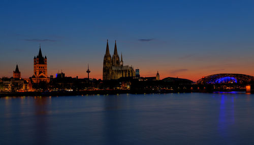 Buildings and cologne cathedral by rhine river in city at night