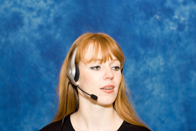 Businesswoman wearing headset in office against blue wall