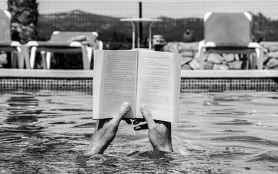 Hands holding novel in swimming pool