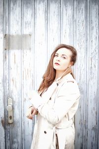 Portrait of young woman wearing overcoat against closed wooden door