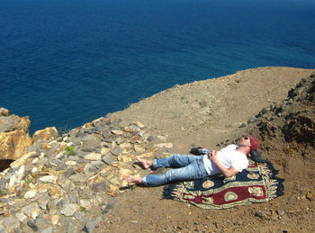 High angle view of man sitting on shore by sea