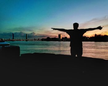 Silhouette man standing by sea against sky during sunset