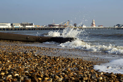 Sea waves splashing on shore against clear sky