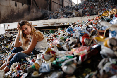 Full length of young woman sitting on garbage