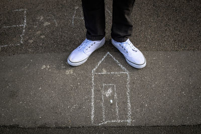 Low section of man standing on road by chalk drawing