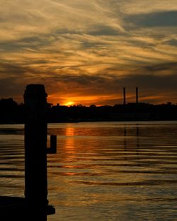 Silhouette wooden posts in calm sea at sunset