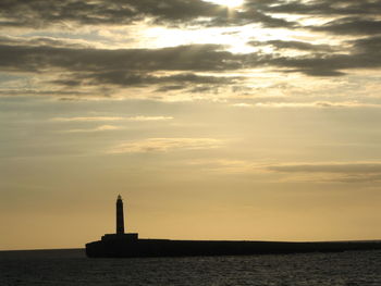 Lighthouse at distance in calm sea against sky