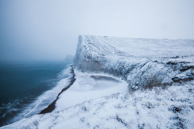 Snow covered cliff by sea