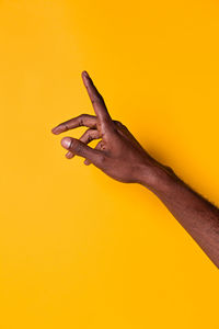 Close-up of hand holding yellow leaf against orange background