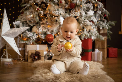 Full length of baby girl sitting on christmas tree at home