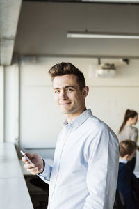 Portrait of smiling man holding smart phone in classroom