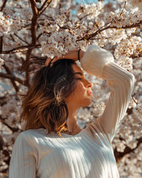 Side view of young woman looking away by flowers on tree