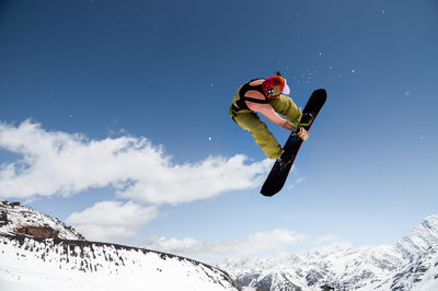 Low angle view of man jumping on snowcapped mountain