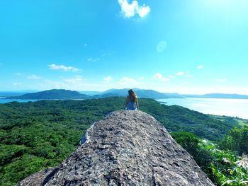 Rear view of woman standing on rock against sky