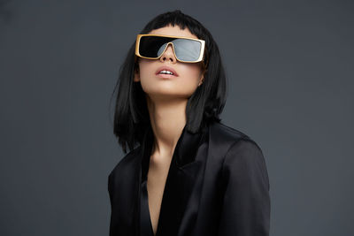 Portrait of young woman wearing sunglasses against black background