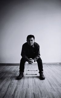 Portrait of young man sitting on wooden wall