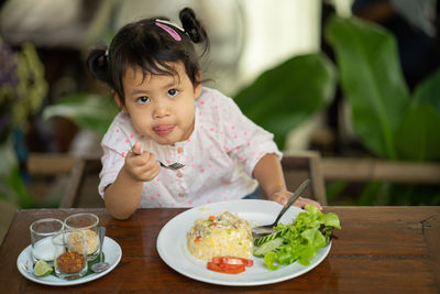 Cute little girl eating fried rice at wooden table.